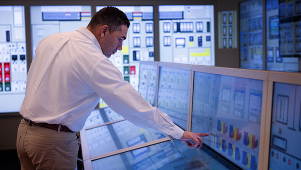 Operator monitoring electrical grid systems and transmission infrastructure on multiple digital displays in the NextEra Energy Transmission control room.