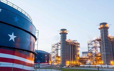 Illuminated natural gas storage tanks painted with an American flag design stand beside modern power generation units at a Florida Power & Light energy facility at dusk