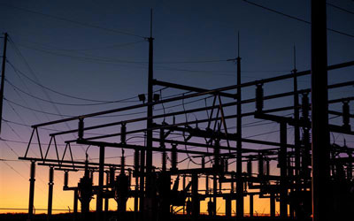 Silhouette of an electrical substation at dusk with wires and pylons.