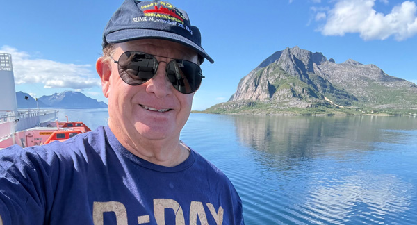 Retiree Coke Coakley smiling on a boat with scenic blue water and mountain landscape in the background.