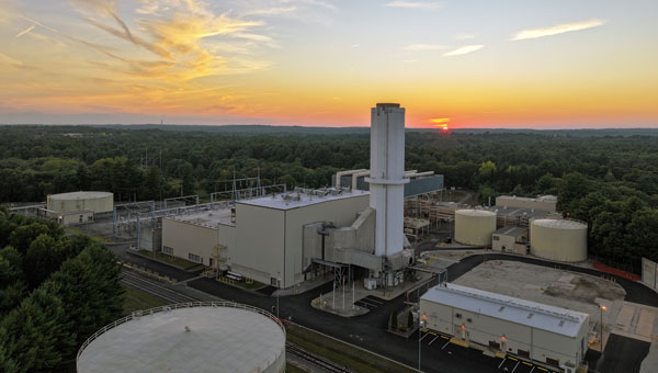 Natural Gas power plant with central stack and storage tanks amid forest at dusk.
